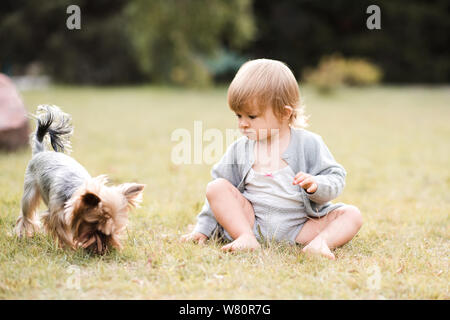 Mignon bébé fille 1-2 ans assis sur l'herbe verte dans le parc avec le chien. L'amitié. La saison d'été. Banque D'Images