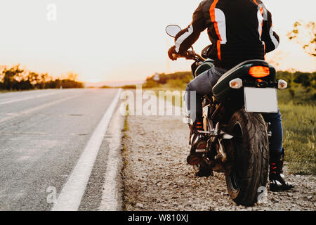 Vue de la récolte d'un motard sur sa moto, de l'arrière lors d'un voyage à préparer pour commencer près de la route contre le coucher du soleil dans son aventure. Banque D'Images