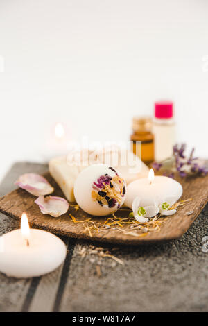 Divers produits de bain spa sur plateau en bois brun crémeux bath bomb, le savon bar avec ficelle en coton, pétales de fleurs séchées, bougies allumées, essentiel spa Banque D'Images