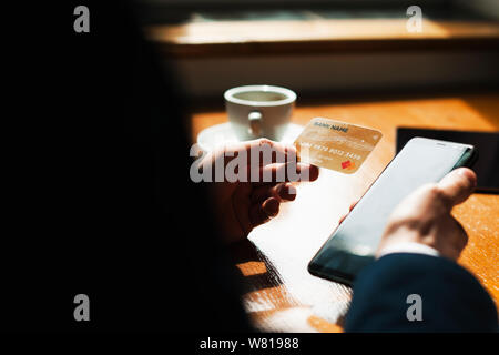 Image main d'hommes cultivés tenant une carte de crédit et un smartphone assis à un bureau dans un café contre une belle lumière. Banque D'Images
