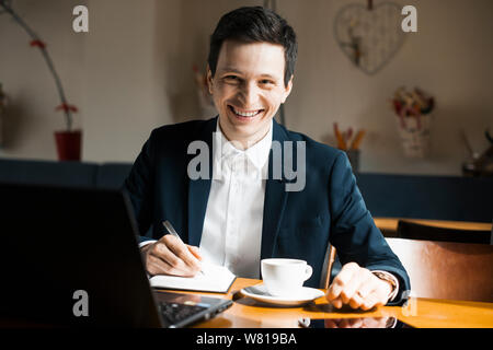 Portrait d'un gestionnaire de race blanche adultes assis à son lieu de travail tout en buvant un café et à la caméra à sourire. Banque D'Images