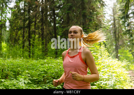 Young woman jogging à travers une forêt ensoleillée Banque D'Images