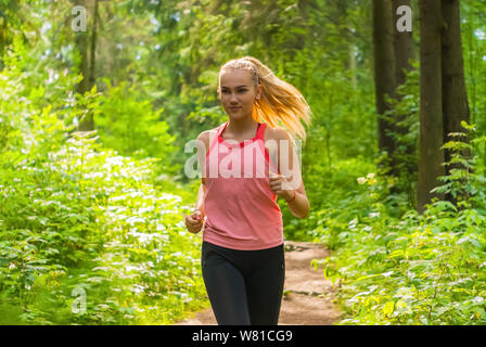 Young woman jogging à travers une forêt ensoleillée Banque D'Images