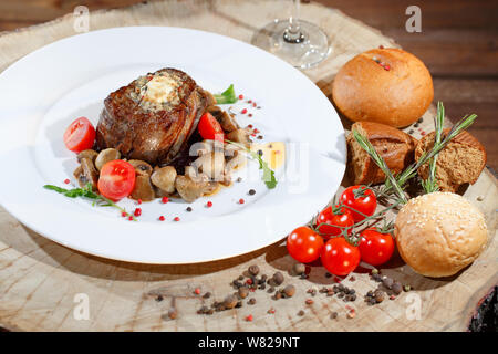 Plat de viande aux champignons sur une plaque blanche sur l'arrière-plan d'une table en bois. Banque D'Images