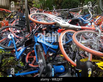 --FILE--endommagée de vélos vélo-partage des services chinois Mobike (orange), ofo (jaune) et Xiaoming Danche, ou Xiaoming Vélo (bleu) sont empilés près de Banque D'Images