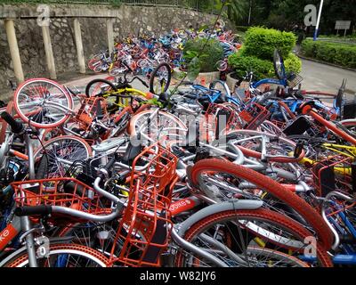 --FILE--endommagée de vélos vélo-partage des services chinois Mobike (orange), ofo (jaune) et Xiaoming Danche, ou Xiaoming Vélo (bleu) sont empilés près de Banque D'Images