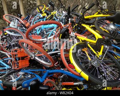 --FILE--endommagée de vélos vélo-partage des services chinois Mobike (orange), ofo (jaune) et Xiaoming Danche, ou Xiaoming Vélo (bleu) sont empilés près de Banque D'Images