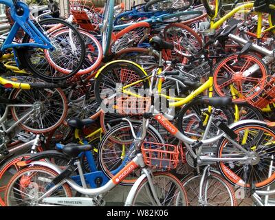 --FILE--endommagée de vélos vélo-partage des services chinois Mobike (orange), ofo (jaune) et Xiaoming Danche, ou Xiaoming Vélo (bleu) sont empilés près de Banque D'Images