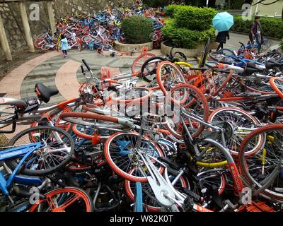 --FILE--endommagée de vélos vélo-partage des services chinois Mobike (orange), ofo (jaune) et Xiaoming Danche, ou Xiaoming Vélo (bleu) sont empilés près de Banque D'Images