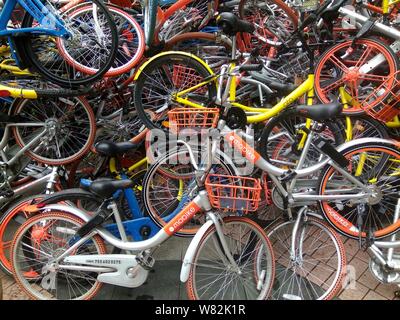 --FILE--endommagée de vélos vélo-partage des services chinois Mobike (orange), ofo (jaune) et Xiaoming Danche, ou Xiaoming Vélo (bleu) sont empilés près de Banque D'Images