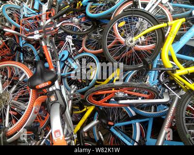 --FILE--endommagée de vélos vélo-partage des services chinois Mobike (orange), ofo (jaune) et Xiaoming Danche, ou Xiaoming Vélo (bleu) sont empilés près de Banque D'Images