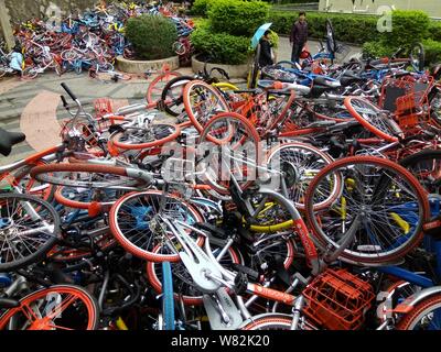 --FILE--endommagée de vélos vélo-partage des services chinois Mobike (orange), ofo (jaune) et Xiaoming Danche, ou Xiaoming Vélo (bleu) sont empilés près de Banque D'Images