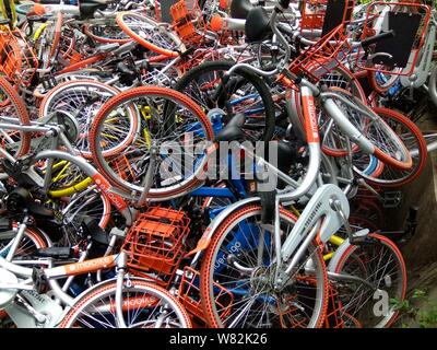 --FILE--endommagée de vélos vélo-partage des services chinois Mobike (orange), ofo (jaune) et Xiaoming Danche, ou Xiaoming Vélo (bleu) sont empilés près de Banque D'Images