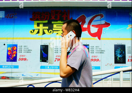 --FILE--un piéton parle sur son téléphone mobile alors qu'il passe devant une publicité pour les services 4G de China Mobile dans la ville de Yichang, Chine centrale's Hube Banque D'Images