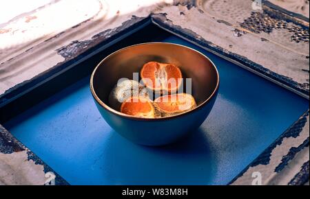 Photographie abstraite de mandarines plaquées en métal dans un bol une surface bleue et en bois Banque D'Images