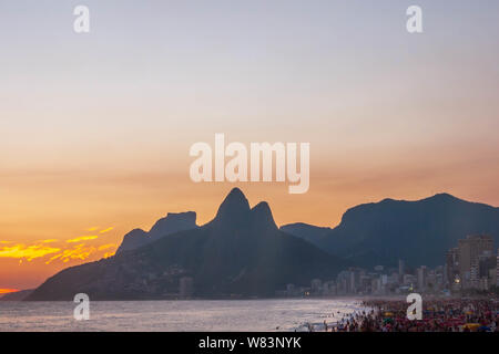 Incroyable coucher du soleil à Rio de Janeiro litoral vu de rock de l'Arpoador illustrant la plage d'Ipanema avec une foule sur le sable et la silhouette des montagnes Banque D'Images