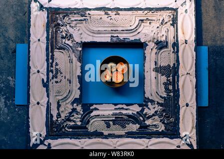 Photographie abstraite de mandarines plaquées en métal dans un bol une surface bleue et en bois Banque D'Images