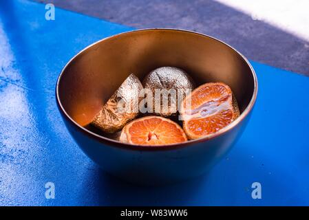 Photographie abstraite de mandarines plaquées en métal dans un bol une surface bleue et en bois Banque D'Images