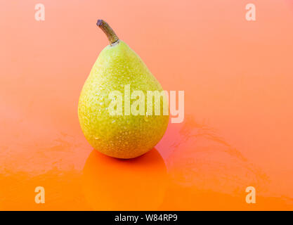 Une douce poire mûre avec des gouttes d'eau sur le dessus, sur un fond orange - poire fraîchement récolté savoureux Banque D'Images