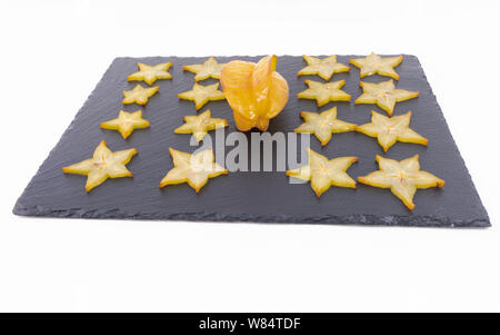 Et Tropical star fruits mûrs sont tranchés et ensemble sur une planche à découper noire sur fond blanc - Carambole Averrhoa Carambola - Mûres Banque D'Images