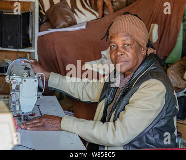 Windhoek, Afrique du Sud - Juillet 6, 2018 : un tailleur coud des vêtements pour la vente dans une minuscule boutique en Namibie Banque D'Images