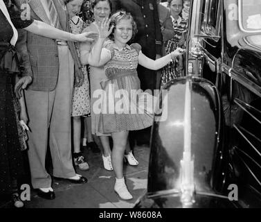 Vintage photo d'enfant américain film star Shirley Temple (1928 - 2014). La photo a été prise le 24 juin 1938 que la jeune actrice fait signe aux spectateurs après avoir quitté la Maison Blanche à la suite d'une réunion avec le président américain Franklin D. Roosevelt. Au cours de leur conversation, elle a dit au président comment elle avait perdu une dent la nuit avant qu'il ne tombe que lorsqu'elle a mangé un sandwich. Banque D'Images