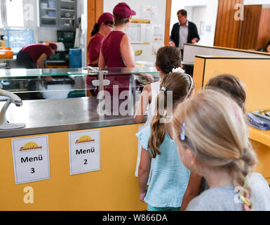 07 août 2019, Berlin : avant le déjeuner, les élèves se tenir dans la cafétéria de l'école primaire sur le Wuhlheide dans la file d'en face de l'comptoir d'alimentation. Photo : Jens Kalaene Zentralbild-/dpa/ZB Banque D'Images