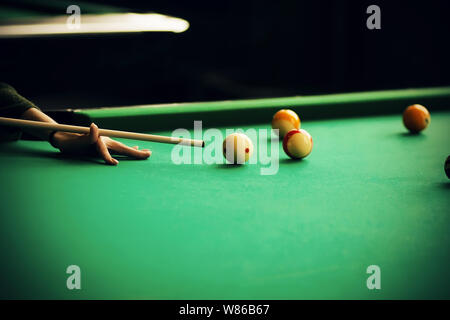 Une femme dans un chandail vert est titulaire d'un cue et vise à une boule de billard, qui est parmi les autres balles sur le green table de billard. Banque D'Images