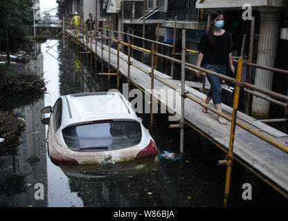 Les résidents locaux chinois marche sur un temorary bridge à côté de voitures privées submergées par l'eau à un quartier résidentiel gorgé de Wuhan City, central Banque D'Images