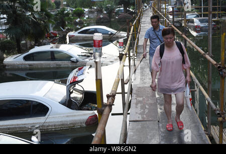 Les résidents locaux chinois marche sur un temorary bridge à côté de voitures privées submergées par l'eau à un quartier résidentiel gorgé de Wuhan City, central Banque D'Images