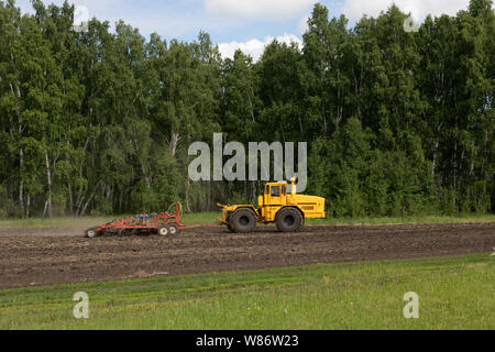 Un tracteur laboure un champ jaune, des herses et cultive le sol pour le semis des céréales. Le concept de l'agriculture et des machines agricoles sur la zone. Banque D'Images