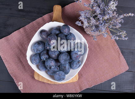 Beaucoup de prunes fraîches dans une assiette blanche sur une table en bois foncé Banque D'Images