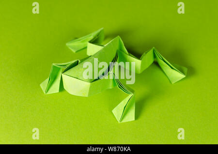 Origami Grenouille verte sur fond vert. L'art japonais du pliage de papier. Feuille de papier carré plat transférés dans la sculpture terminée par le pliage. Banque D'Images