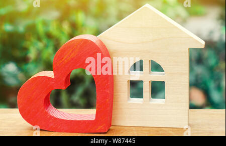 Maison avec un coeur en bois rouge sur un fond vert. Chambre des amoureux. Logement à prix abordable pour les jeunes familles. 'Home Sweet Home' de l'assurance-vie. Banque D'Images