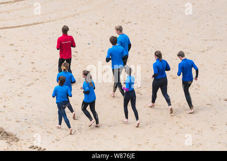 Les surfeurs débutants se réchauffer avec leur moniteur avant une leçon de surf sur une grande Gt. Plage de l'ouest à Newquay en Cornouailles. Banque D'Images