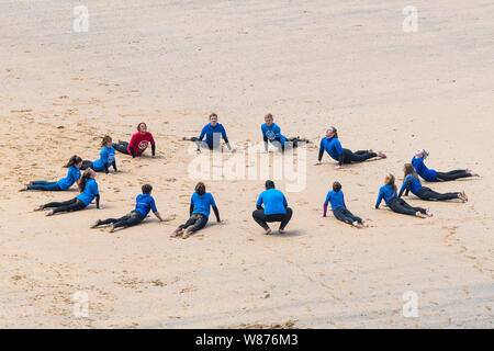 Les surfeurs débutants l'échauffement avant une leçon de surf sur une grande Gt. Plage de l'ouest à Newquay en Cornouailles. Banque D'Images