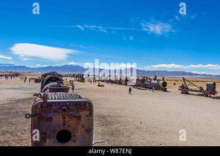 Cimetière de train, Uyuni, Bolivie : vieux abandonnés locomotives à vapeur, trains vintage se coucher sur le sol blanc et certains touristes dans un monument populaire Banque D'Images