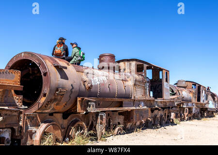 Cimetière de train, Uyuni, Bolivie : vieux abandonnés locomotives à vapeur, trains vintage se coucher sur le sol blanc et certains touristes dans un monument populaire Banque D'Images