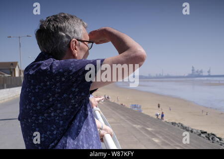 80 yr old man looking out to sea, la retraite à la plage par temps ensoleillé Banque D'Images