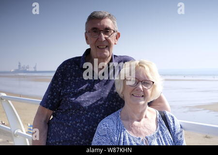 Un couple de personnes âgées à plus jeunes que leurs dernières années, à la recherche de l'appareil photo à la plage avec en arrière-plan Banque D'Images