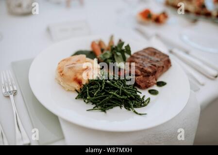 Prise de vue en hauteur d'un steak, de légumes verts et de légumes dans une assiette sur une table de mariage Banque D'Images