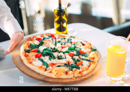 Le serveur met sur la table une pizza au restaurant. Banque D'Images