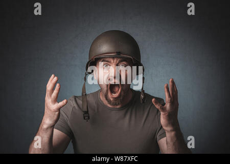 Portrait d'un soldat crier à bras ouverts. Il porte un casque de métal. Banque D'Images