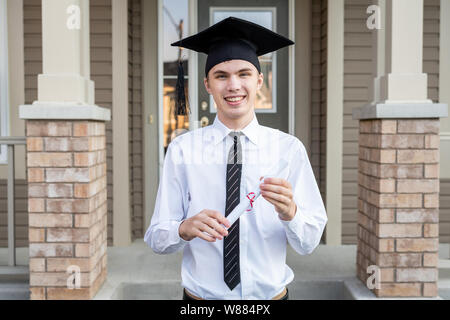 Jeune étudiant titulaire d'un diplôme tout en portant une graduation cap devant une maison. Banque D'Images