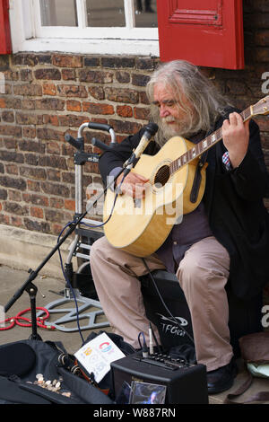 Homme aux longs cheveux gris chantant et jouant de la guitare acoustique dans une rue à York, North Yorkshire, Angleterre, Royaume-Uni. Banque D'Images