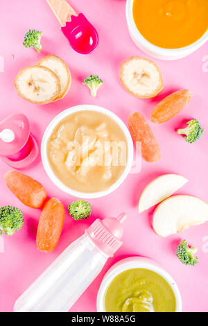 Infant baby food concept. Bols avec purée de fruits Légumes, vert, orange, jaune couleurs - le brocoli, carottes, banane, pomme. Avec bébé et accessoires Banque D'Images