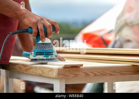 Travailleur Grinder polit une planche de bois. Conseils de ponçage excentrique orbitale machine. Banque D'Images