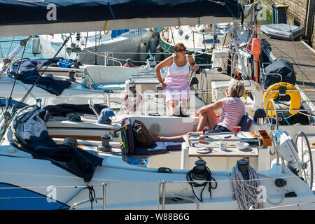 Les femmes riches bavarder après le petit-déjeuner à bord de leurs bateaux à voile yachts / voisins / amarré amarré dans la marina / yacht basin / port en été Banque D'Images