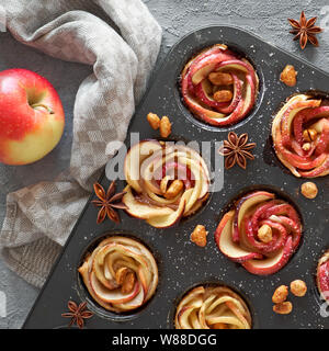 Le bac d'apple en feuilleté au four roses sur fond de béton gris avec les feuilles d'automne et pommes rouges Banque D'Images