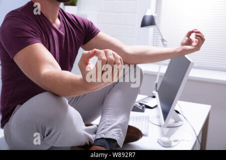 Young Businessman Sitting on Desk In Office Banque D'Images